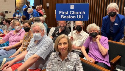 Group of people, some with masks holding a sing reading First CHurch Boston UU