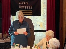 Woman standing at a table speaking holding a piece of paper