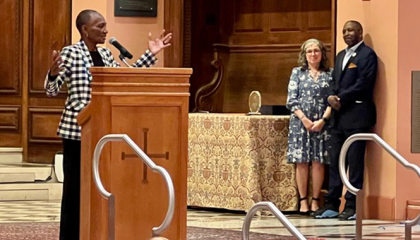 A woman at a podium speaking with a man and woman standing in the background