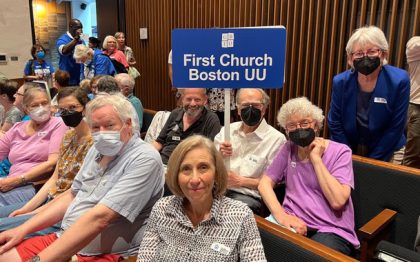 Group of people sitting , many wearing masks, with a sign First Church Boston UU