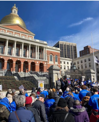 A rally of people in blue shirts outside the MA Statehouse