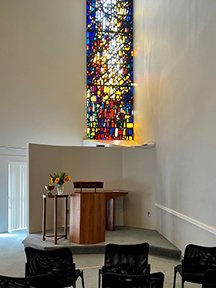 Colorful stained glass window in a white room with lectern and seats