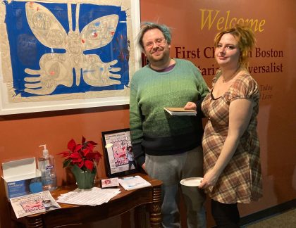 Two people looking at the camera with blue butterfly like artwrk on the wall.