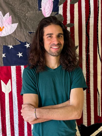 Young man with long dark hair and smiling wearing a dark green T shirt.