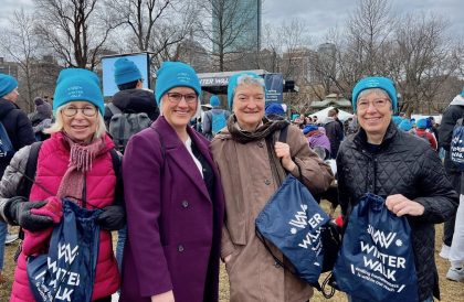 group of women outdoors smiling with turquoise hats and dar blue bags saying Winter Walk
