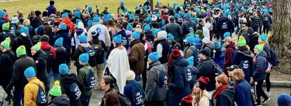 A crowd of people, many with turquoise hats, marching in winter.