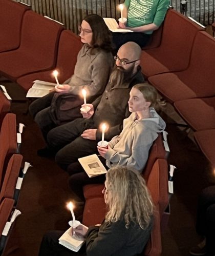 A group of people sitting quietly in a row holding candles.