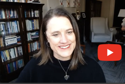 A woman with brown hair in her study with a YouTube play arrow.